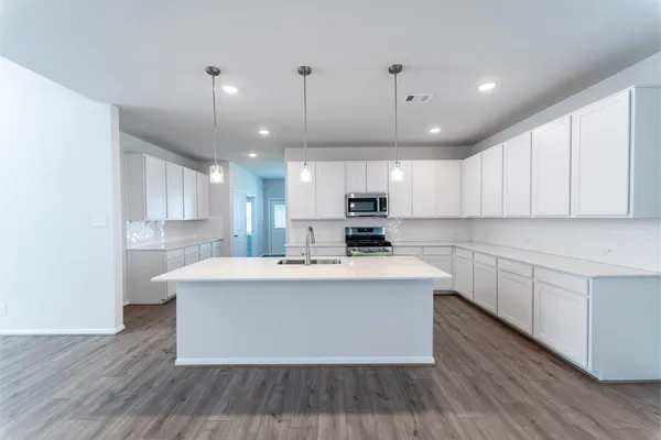 a large kitchen with stainless steel appliances a large kitchen island hardwood floor sink stove and wooden cabinets