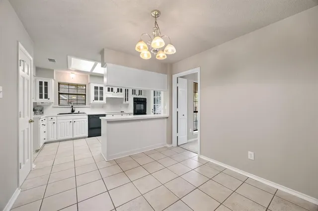 a large white kitchen with cabinets a island a stove a chimney and a chandelier