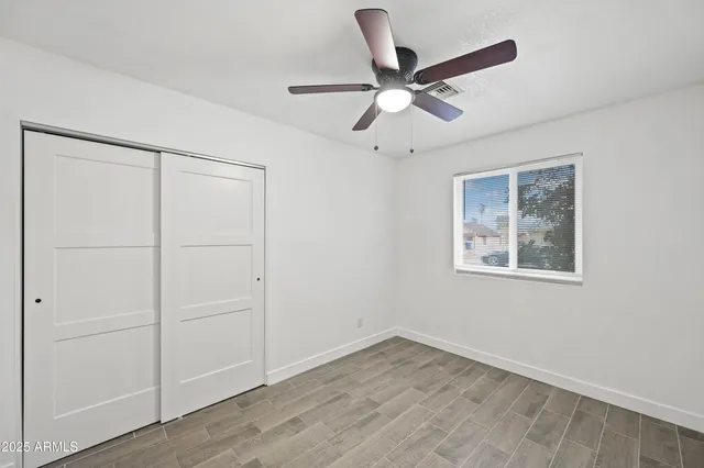 an empty room with wooden floor closet and ceiling fan