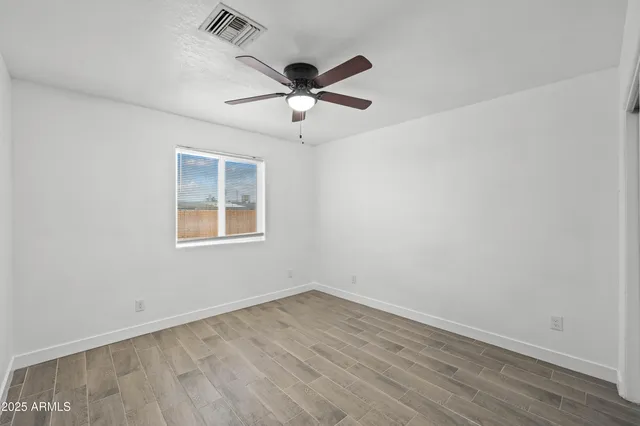 an empty room with wooden floor fan and windows