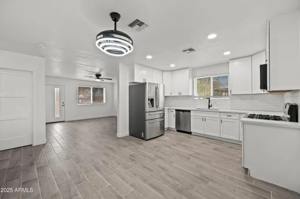 a kitchen with stainless steel appliances granite countertop a refrigerator a sink dishwasher a stove and white countertops with wooden floor