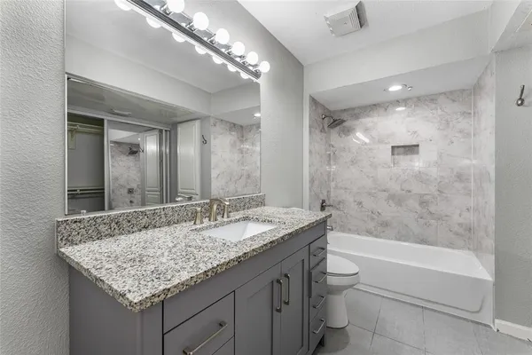 a bathroom with a granite countertop sink a toilet a mirror and bathtub