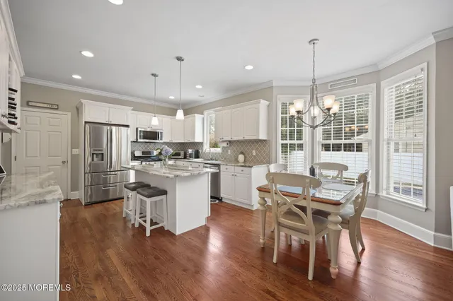 a kitchen with stainless steel appliances kitchen island granite countertop a refrigerator a sink dishwasher a stove and white countertops with wooden floor