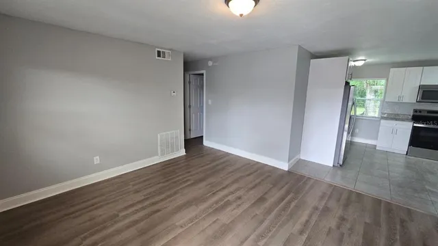 an empty room with wooden floor kitchen view and windows