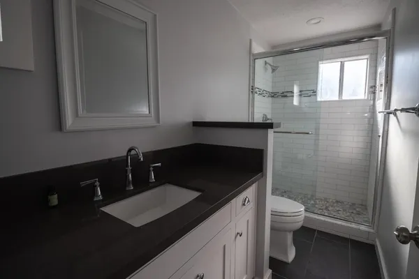 a bathroom with a granite countertop sink toilet a mirror and shower