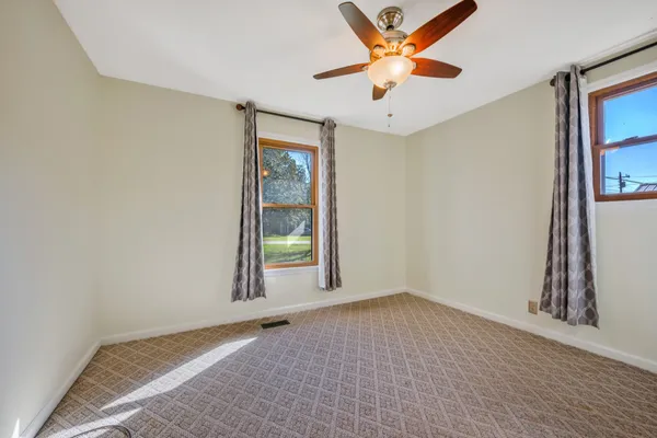 an empty room with chandelier fan and windows