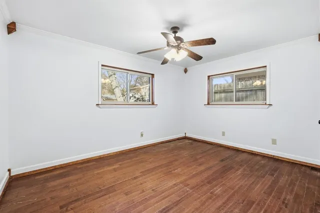 a view of an empty room with wooden floor and a ceiling fan