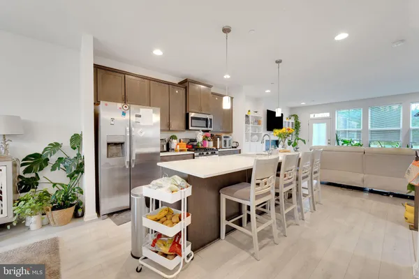 a kitchen with stainless steel appliances kitchen island granite countertop a refrigerator a stove a sink a dining table and chairs with wooden floor