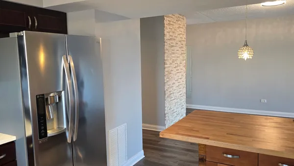 a view of an empty room with wooden floor and a kitchen