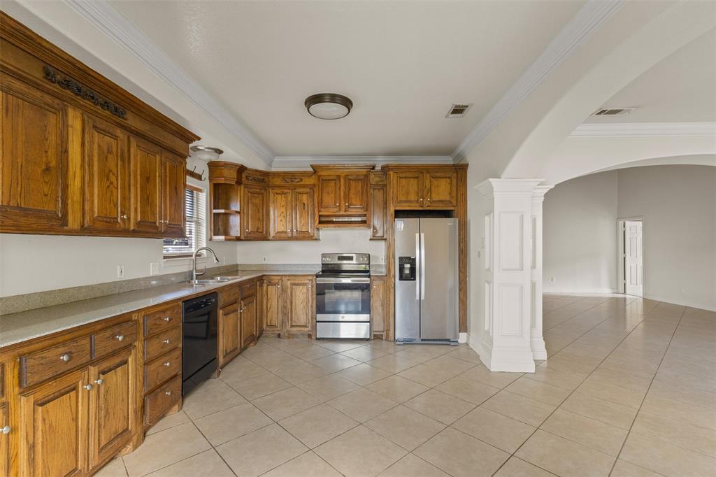 490 Lynne Drive Rockwall, TX 75032 - Photo 11 of 27 Kitchen featuring crown molding, light tile patterned floors, brown cabinetry, appliances with stainless steel finishes, and arched walkways
