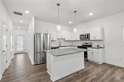 a kitchen with stainless steel appliances granite countertop a refrigerator a sink dishwasher a stove and white cabinets with wooden floor