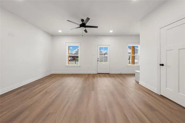 an empty room with wooden floor chandelier fan and windows