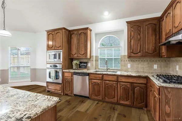 a kitchen with stainless steel appliances granite countertop a stove top oven a sink dishwasher and wooden cabinets with wooden floor