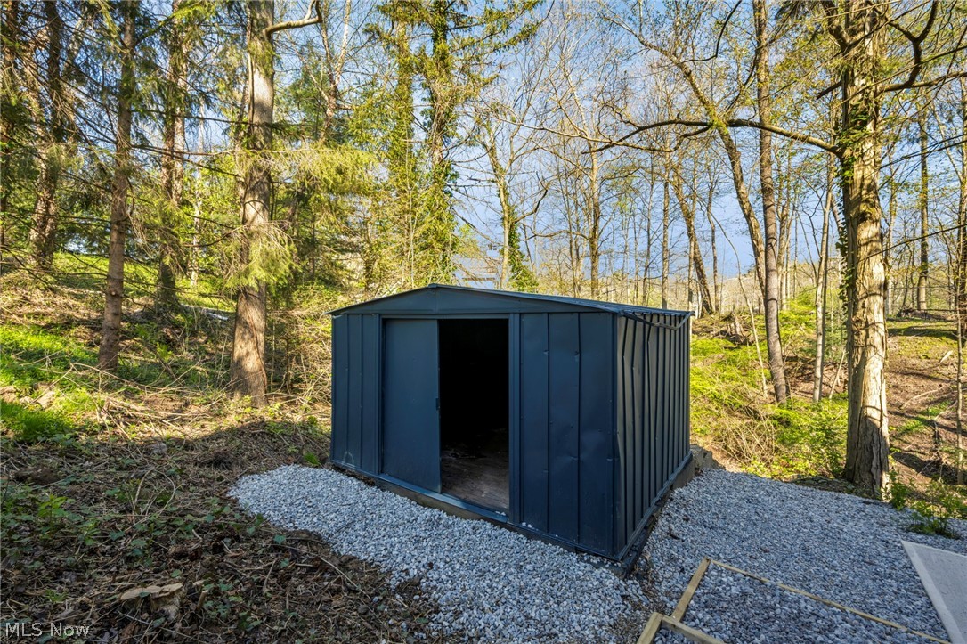 7339 River Road Olmsted Falls, OH 44138 - Photo 42 of 45 Gray metal storage shed with an open doorway, situated on a gravel pad