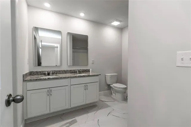 a bathroom with a granite countertop toilet a sink and a mirror