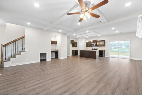 an empty room with wooden floor kitchen view and a window