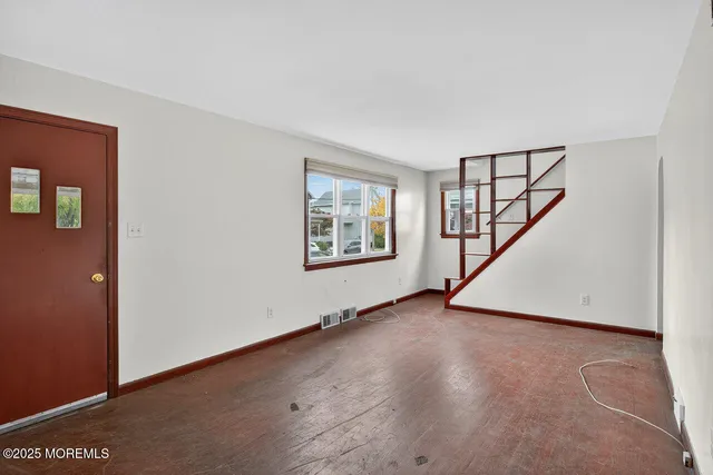 a view of an empty room with wooden floor and stairs