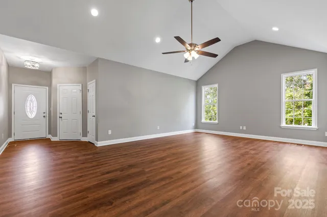 an empty room with wooden floor chandelier fan and windows