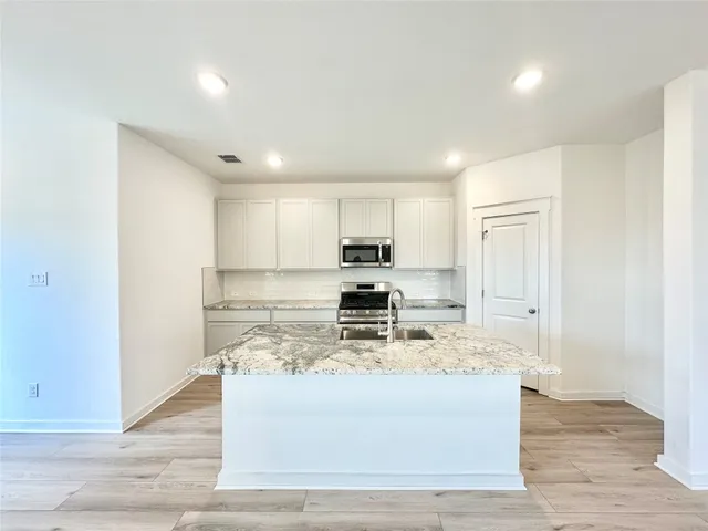 a view of kitchen with stainless steel appliances granite countertop refrigerator stove microwave and cabinets
