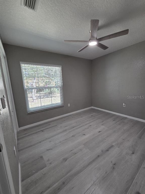 Undisclosed Address Spring Hill, FL 34609 - Photo 37 of 50 an empty room with wooden floor chandelier fan and windows
