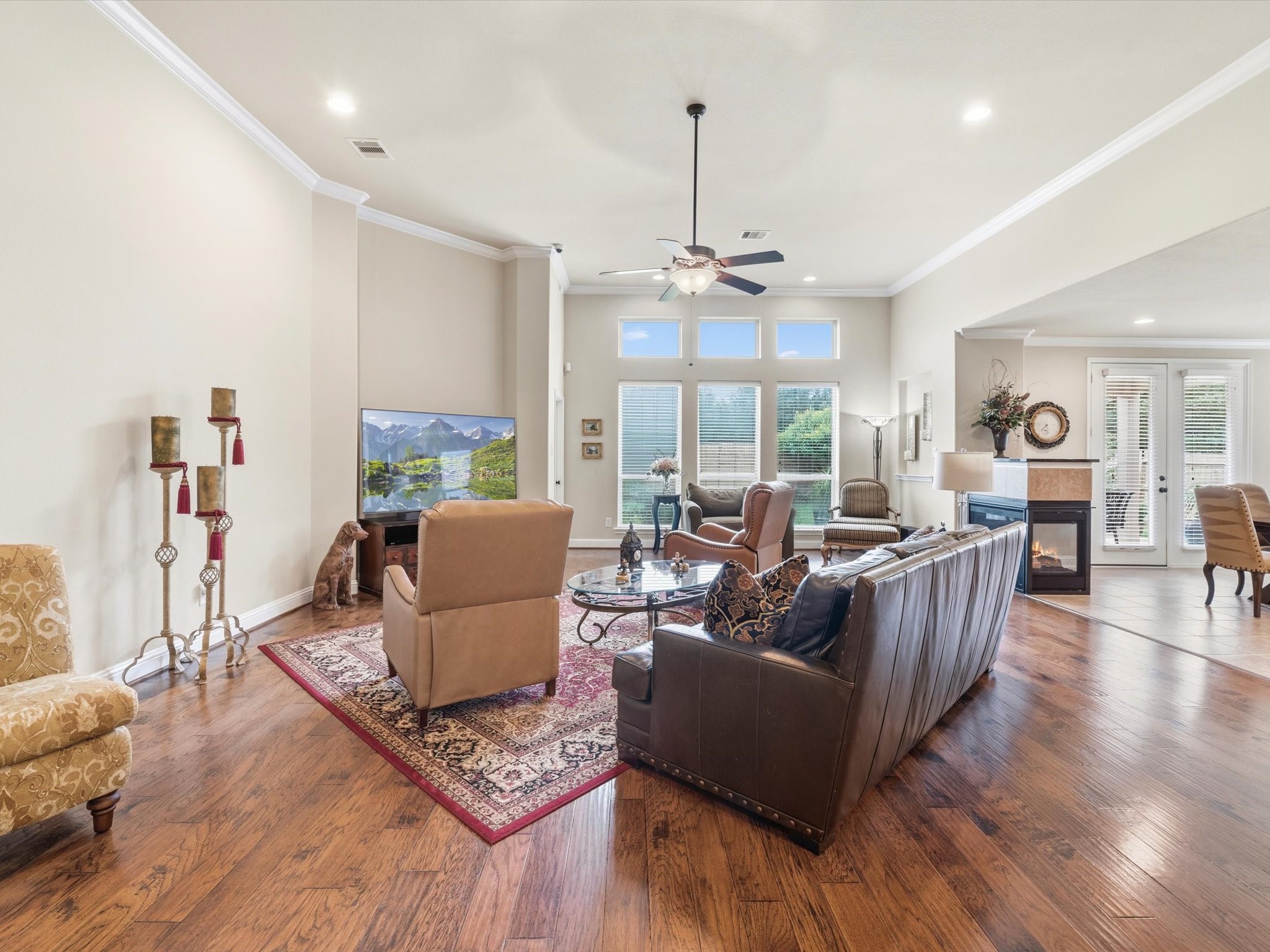 3907 Randle Ridge Court Fulshear, TX 77441 - Photo 8 of 46 Another view of the living area features hardwood floors, high ceilings, and large windows that let in plenty of natural light. It includes a cozy seating area with a fireplace and a view of the backyard.