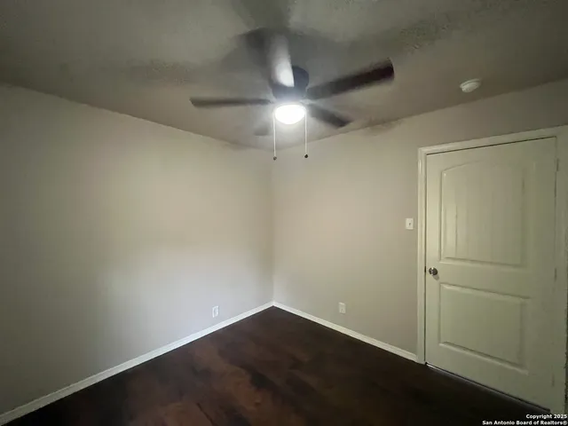 an empty room with wooden floor and fan