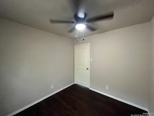 an empty room with wooden floor and fan