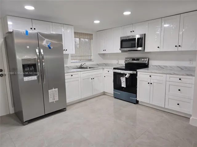 a large kitchen with stainless steel appliances granite countertop a refrigerator sink and white cabinets