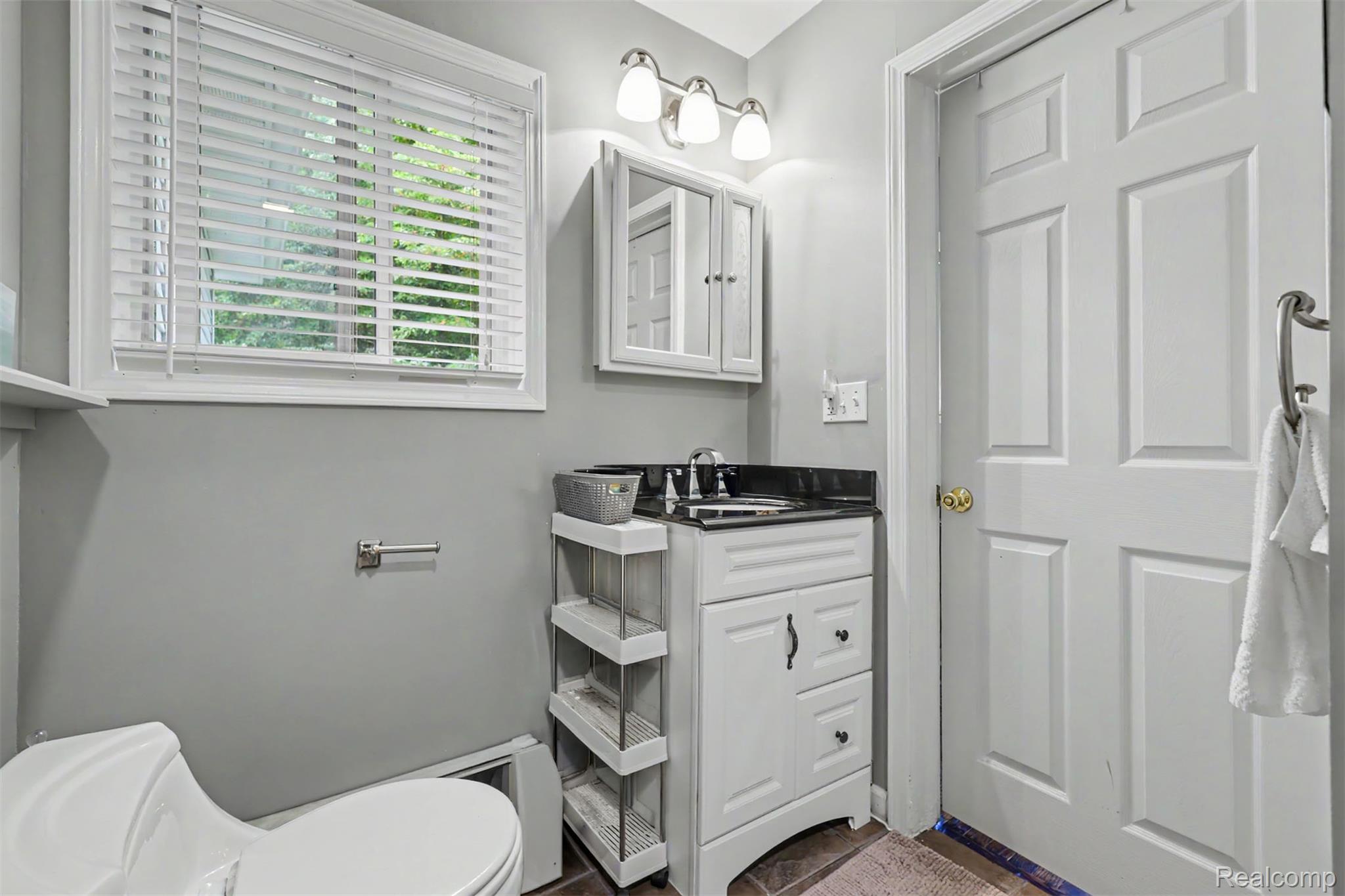 45223 Wear Road Belleville, MI 48111 - Photo 43 of 60 Window with white blinds, white vanity with black countertop, white medicine cabinet, and three-light fixture