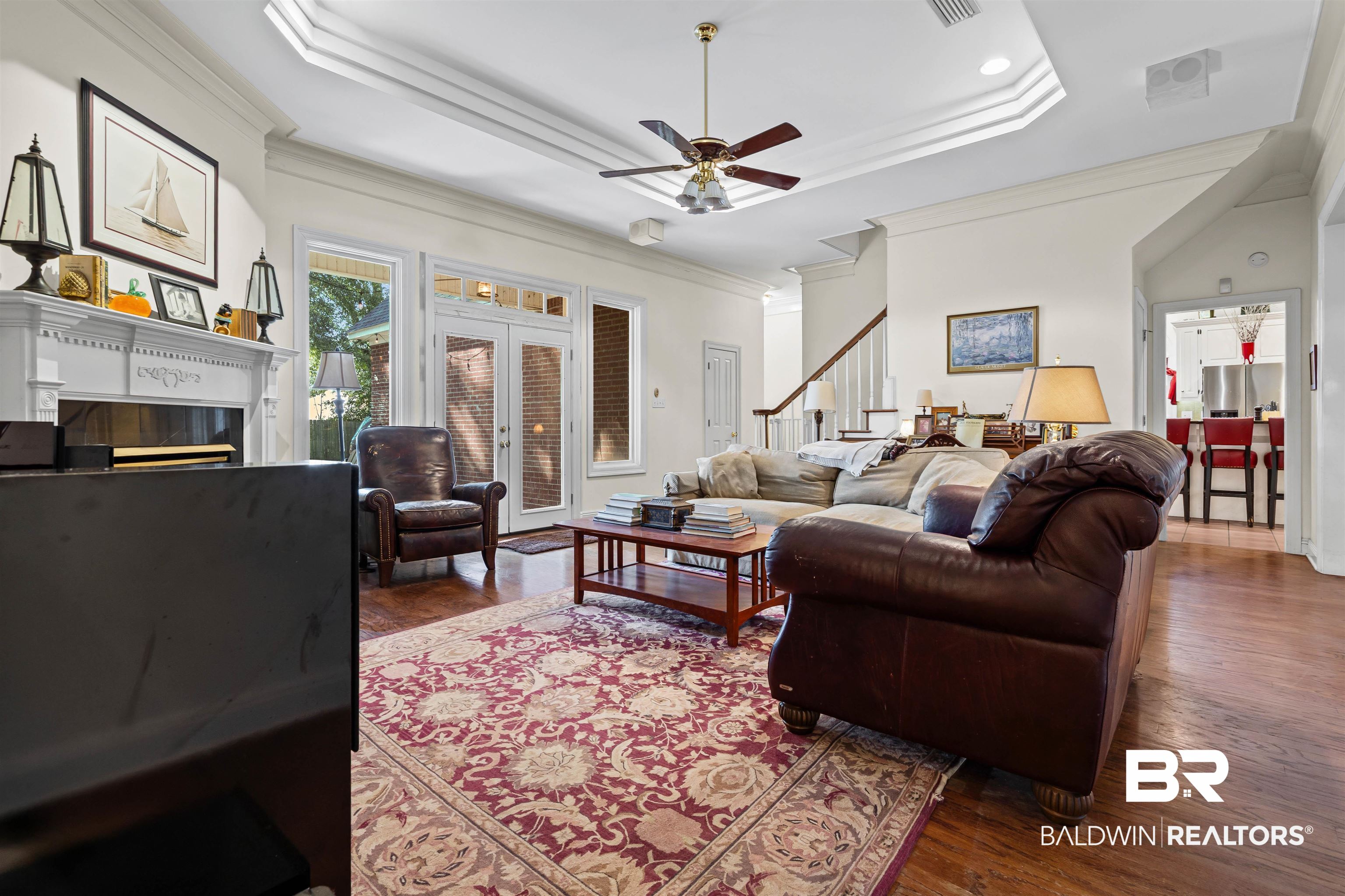107 Beaver Dam Road Fairhope, AL 36532 - Photo 16 of 45 Living area featuring a raised ceiling, a glass covered fireplace, ornamental molding, dark wood-type flooring, and a ceiling fan