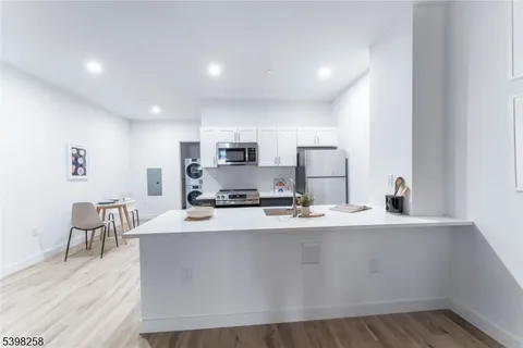 a kitchen with stainless steel appliances a sink a stove a refrigerator with white cabinets and wooden floor