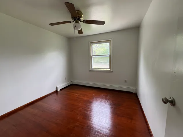 an empty room with wooden floor fan and windows