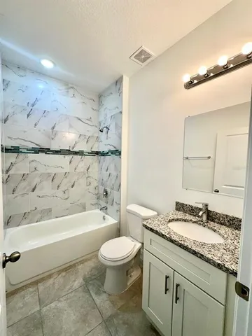 a bathroom with a granite countertop sink a toilet a mirror and bathtub