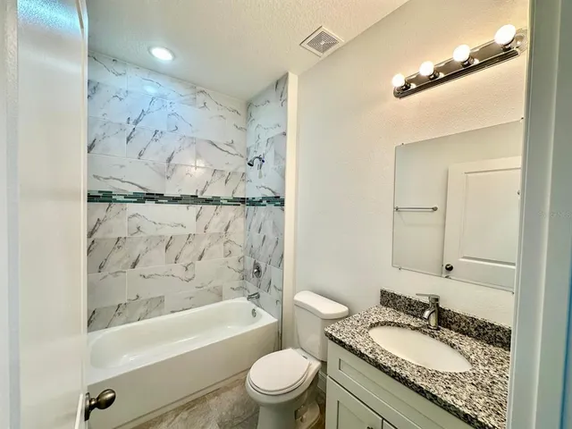 a bathroom with a granite countertop sink a toilet a mirror a vanity and bathtub
