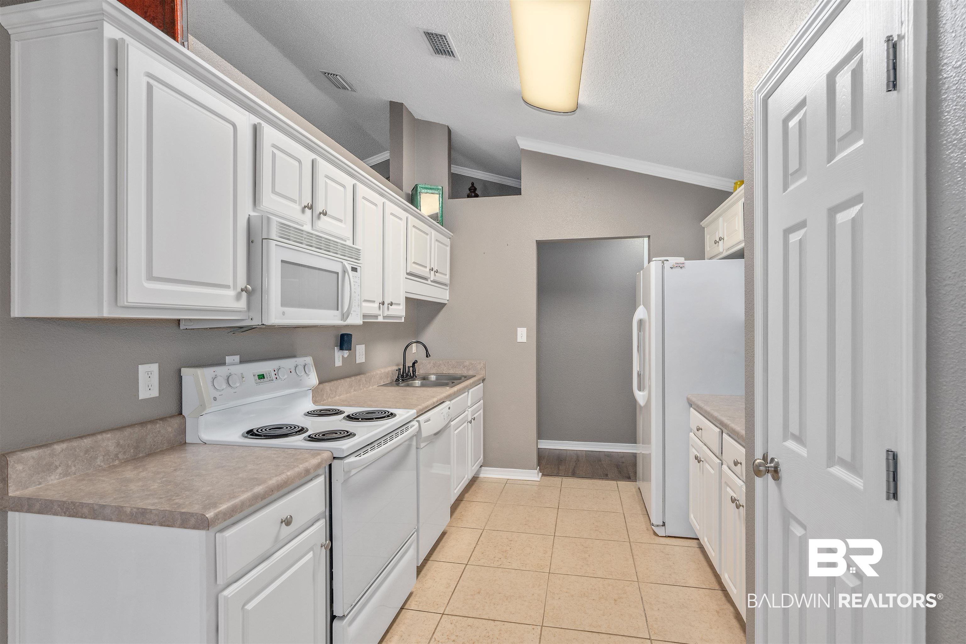 11097 Pontchartrain Loop Daphne, AL 36526 - Photo 10 of 28 Kitchen with white appliances, ornamental molding, white cabinetry, light tile patterned flooring, and lofted ceiling