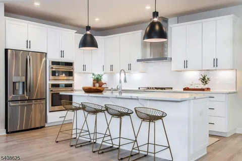 a kitchen with stainless steel appliances a stove a refrigerator and white cabinets with wooden floors