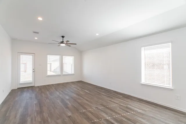 an empty room with wooden floor ceiling fan and windows