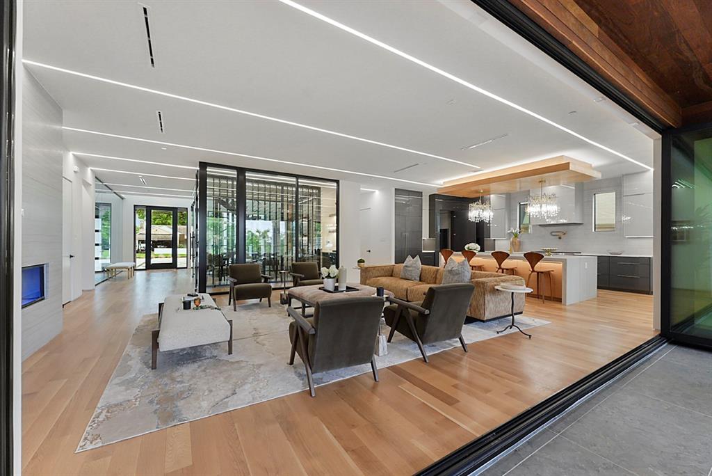 9457 Waterview Road Dallas, TX 75218 - Photo 9 of 25 Open-concept living space featuring wood-finish flooring, linear ceiling lighting, a built-in fireplace, a glass-enclosed feature wall, and a kitchen with an island and pendant lighting