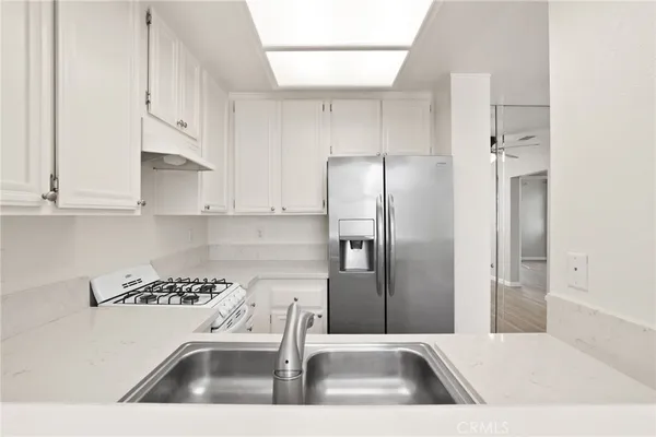 a kitchen with stainless steel appliances granite countertop a refrigerator a sink and white cabinets