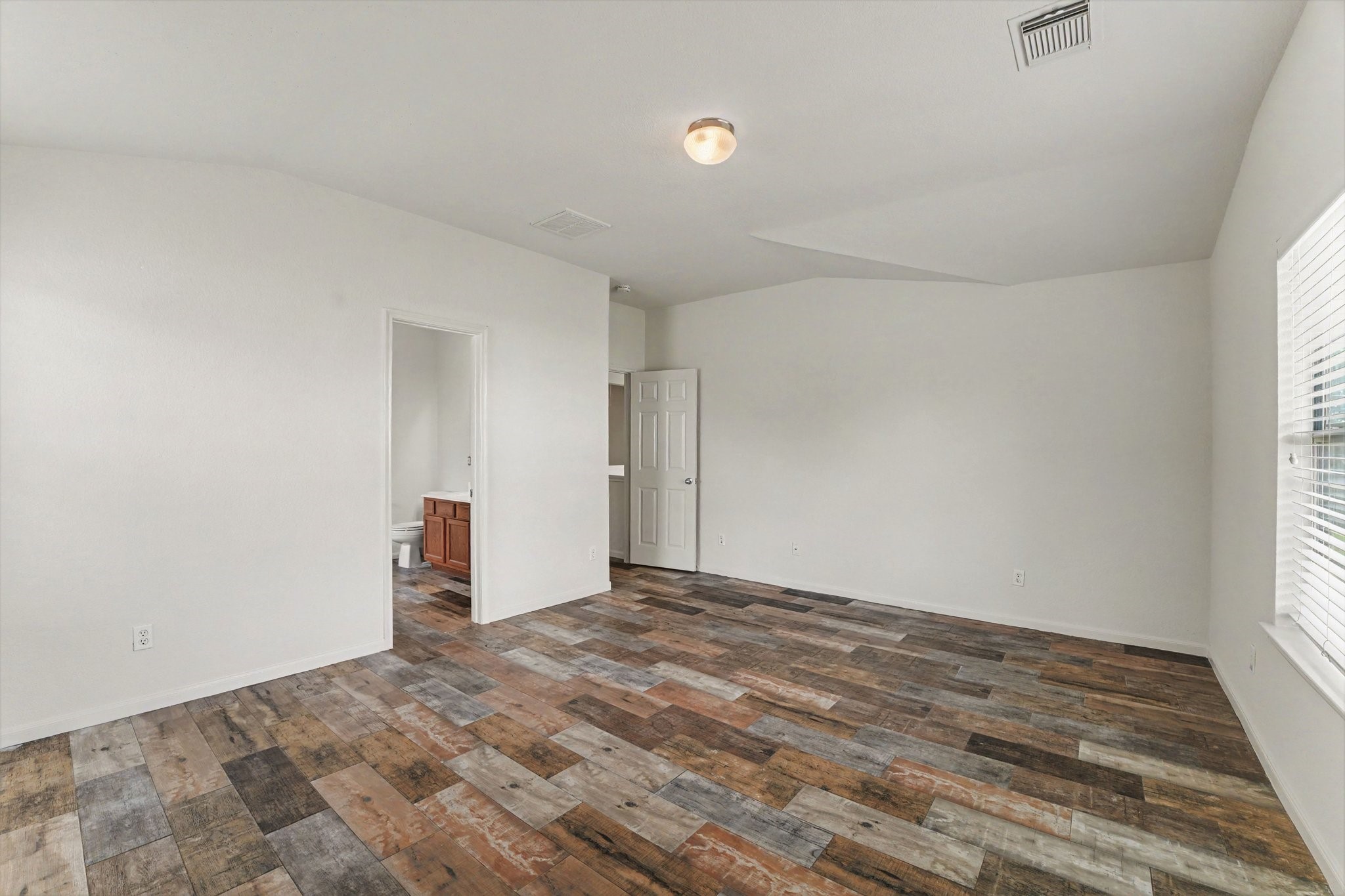 21427 Blooming Rock Lane Spring, TX 77379 - Photo 18 of 32 This room features a bright, open space with light-colored walls and a unique, multi-toned wood floor. A doorway leads to an adjacent room with a visible vanity, and a window allows natural light to fill the space.