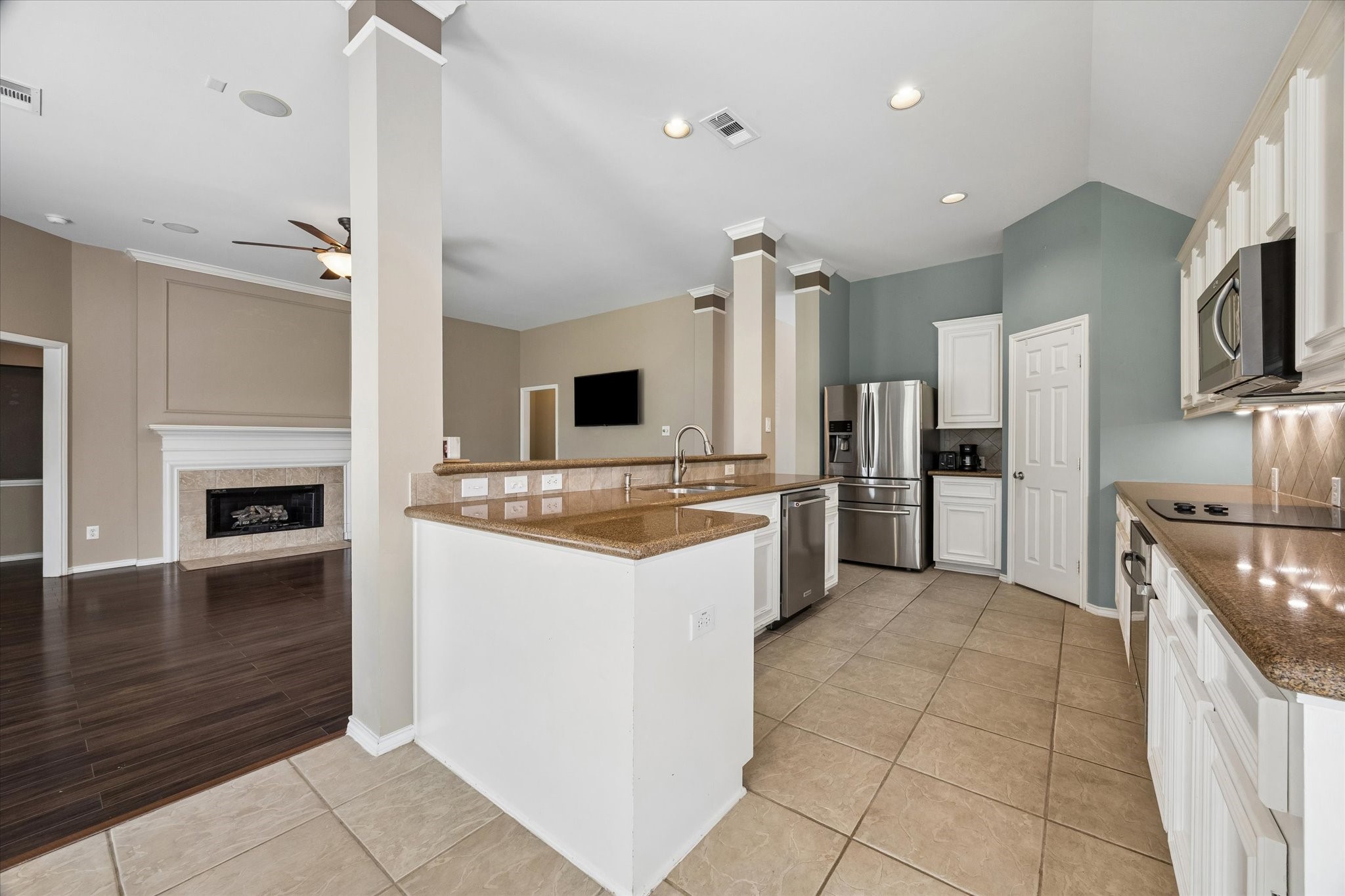 3118 Valley Court Manvel, TX 77578 - Photo 9 of 38 This photo showcases a spacious, open-concept kitchen and living area. The kitchen features modern stainless steel appliances, ample counter space, and a large island with a sink. Adjacent is a cozy living space with a fireplace and hardwood flooring, perfect for entertaining or family gatherings.