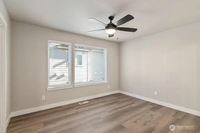 an empty room with wooden floor fan and windows