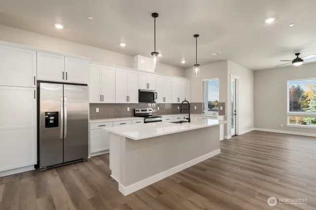 a kitchen with stainless steel appliances kitchen island a sink a refrigerator a stove and white cabinets with wooden floor