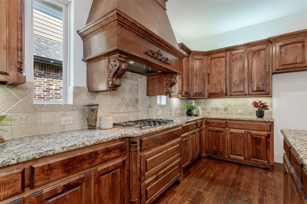 846 Deerfield Road Allen, TX 75013 - Photo 15 of 40 Wood cabinetry, granite countertops, decorative range hood, gas cooktop, and tile backsplash
