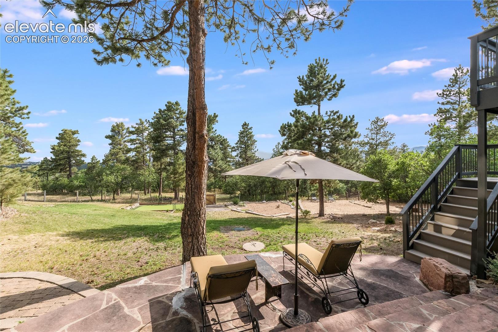 12730 Bridle Bit Road Colorado Springs, CO 80908 - Photo 26 of 48 Stone patio with irregular flagstone pavers, surrounded by mature trees and a natural landscape