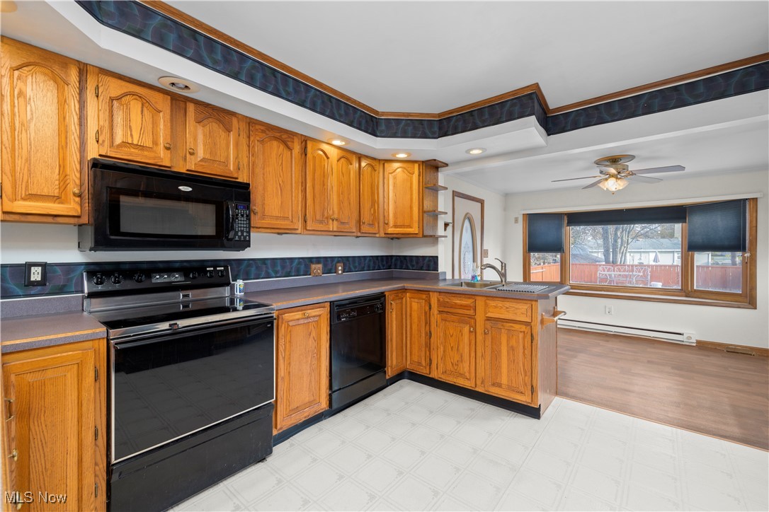 2156 South Oldgate Road Sandusky, OH 44870 - Photo 2 of 6 Kitchen featuring black appliances, brown cabinetry, light flooring, a peninsula, and a baseboard radiator