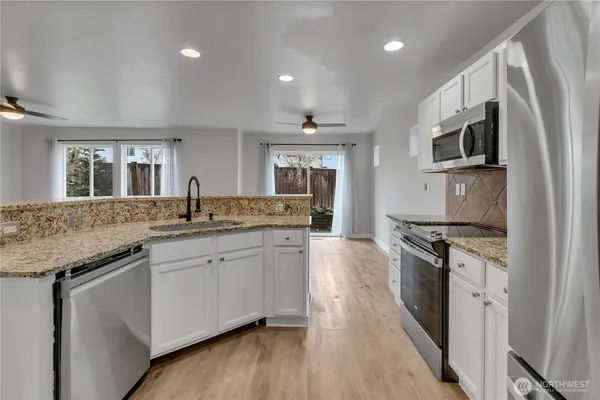 a kitchen with stainless steel appliances granite countertop a stove top oven a sink dishwasher a refrigerator and a oven with wooden floor