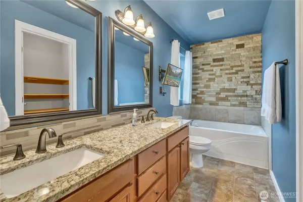 a bathroom with a granite countertop double vanity sink toilet mirror and bathtub