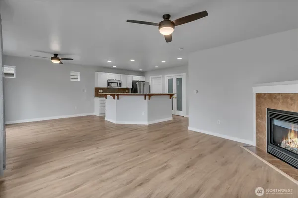 an empty room with wooden floor fireplace and a kitchen view