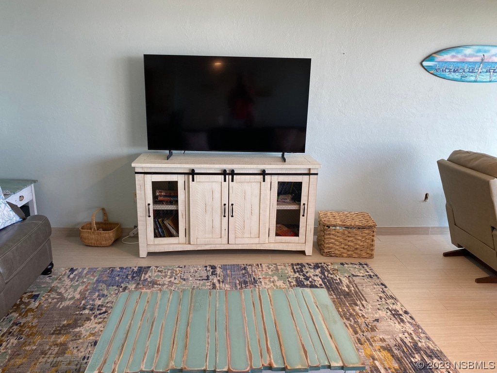 6727 Turtlemound Road, Unit 416 New Smyrna Beach, FL 32169 - Photo 16 of 67 a living room with a flat screen tv on dresser and a table with wooden floor